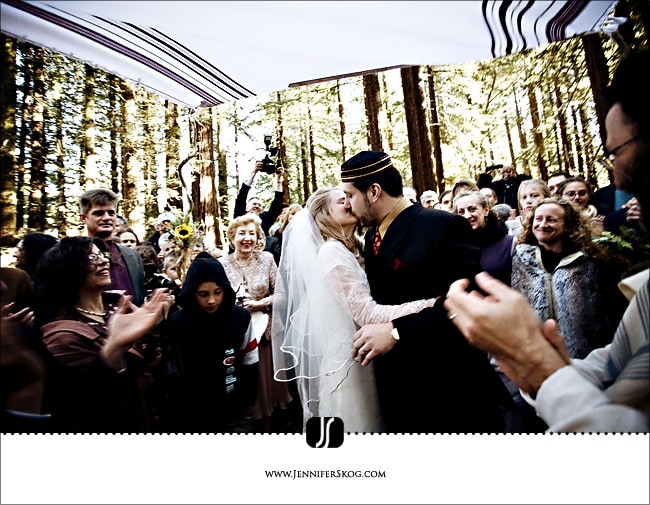 Bride and Groom kiss under the chuppah surrounded by friends in a Redwood Grove - Oakland Wedding