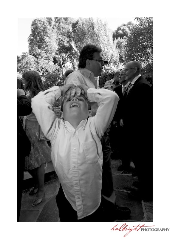 Boy dressed in white dress shirt at wedding with his dad's hand on his forehead