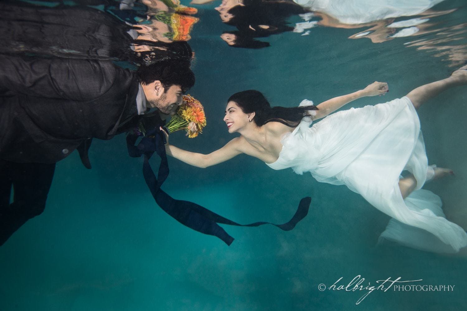 Bride and groom photographed underwater with bouquet