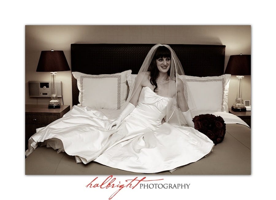 Bride showing off her beautiful wedding dress while sitting on her hotel room bed | San Jose Wedding - Bride on hotel bed - Bay Area Wedding Photographer